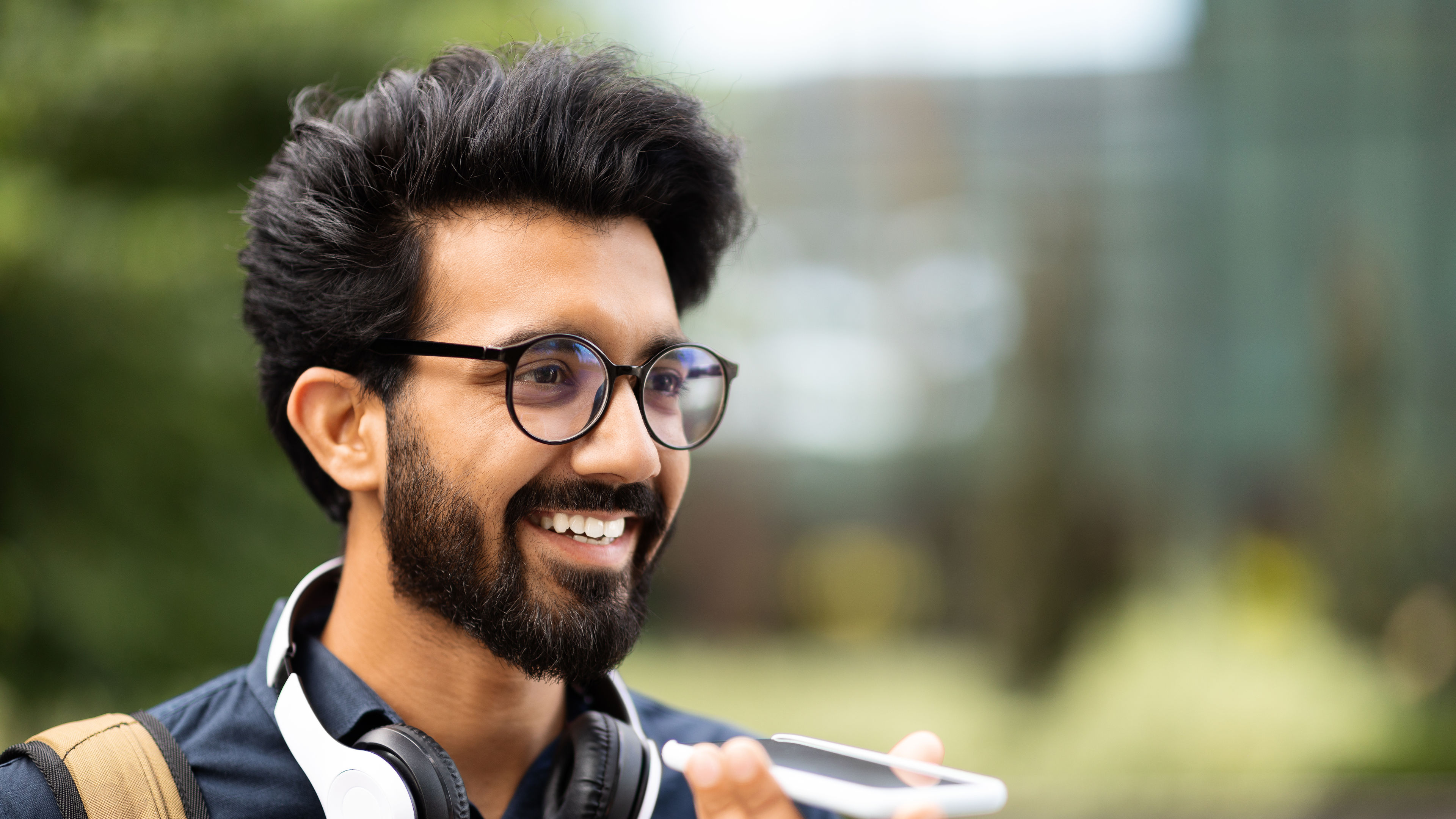 Cheerful indian guy recording voicemail on phone, walking by street