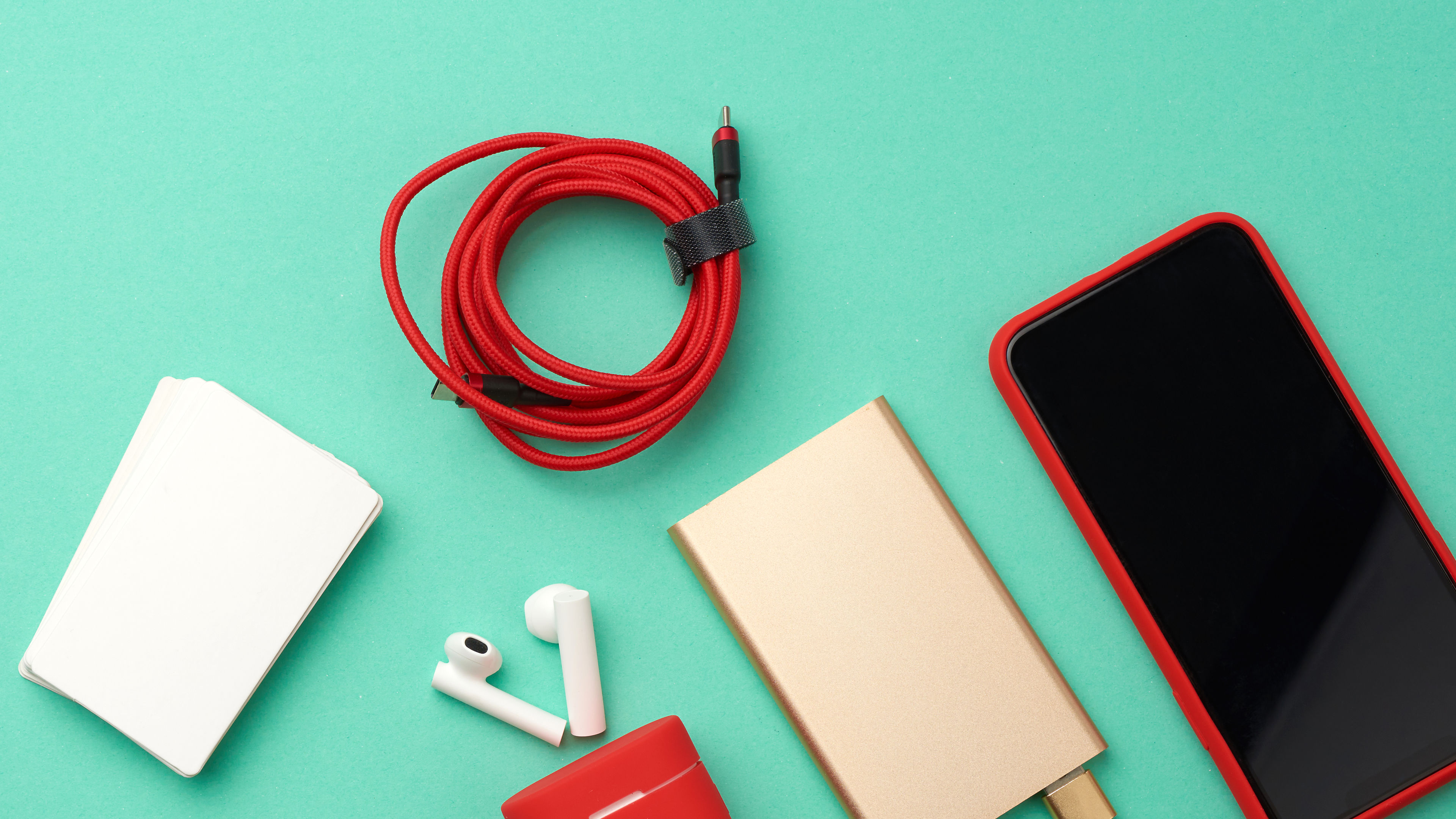 Golden power bank with cable, red smartphone with blank black screen, box with headphones, empty paper business cards on green background