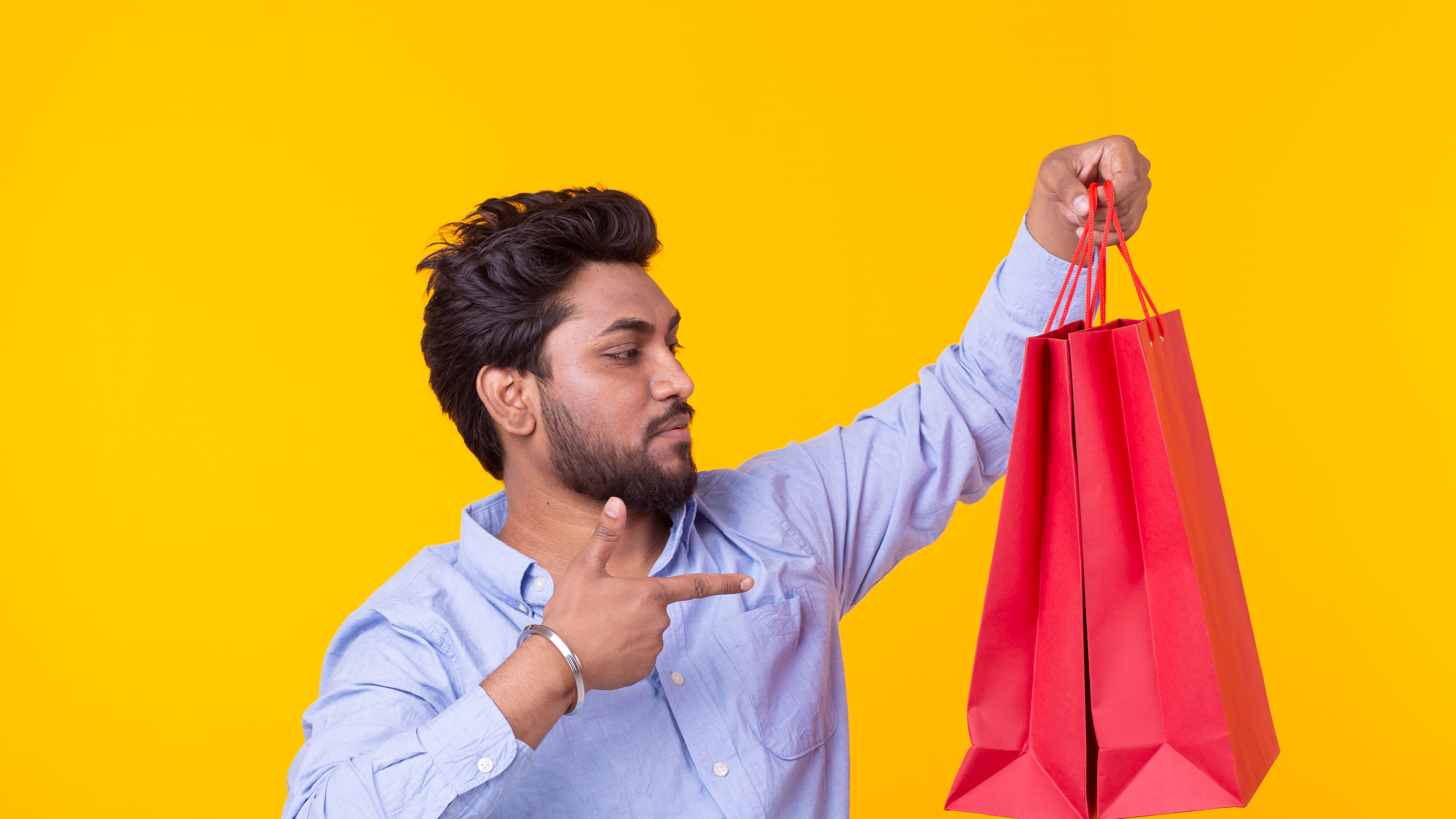 Indian man with a beard is holding red shopping bags