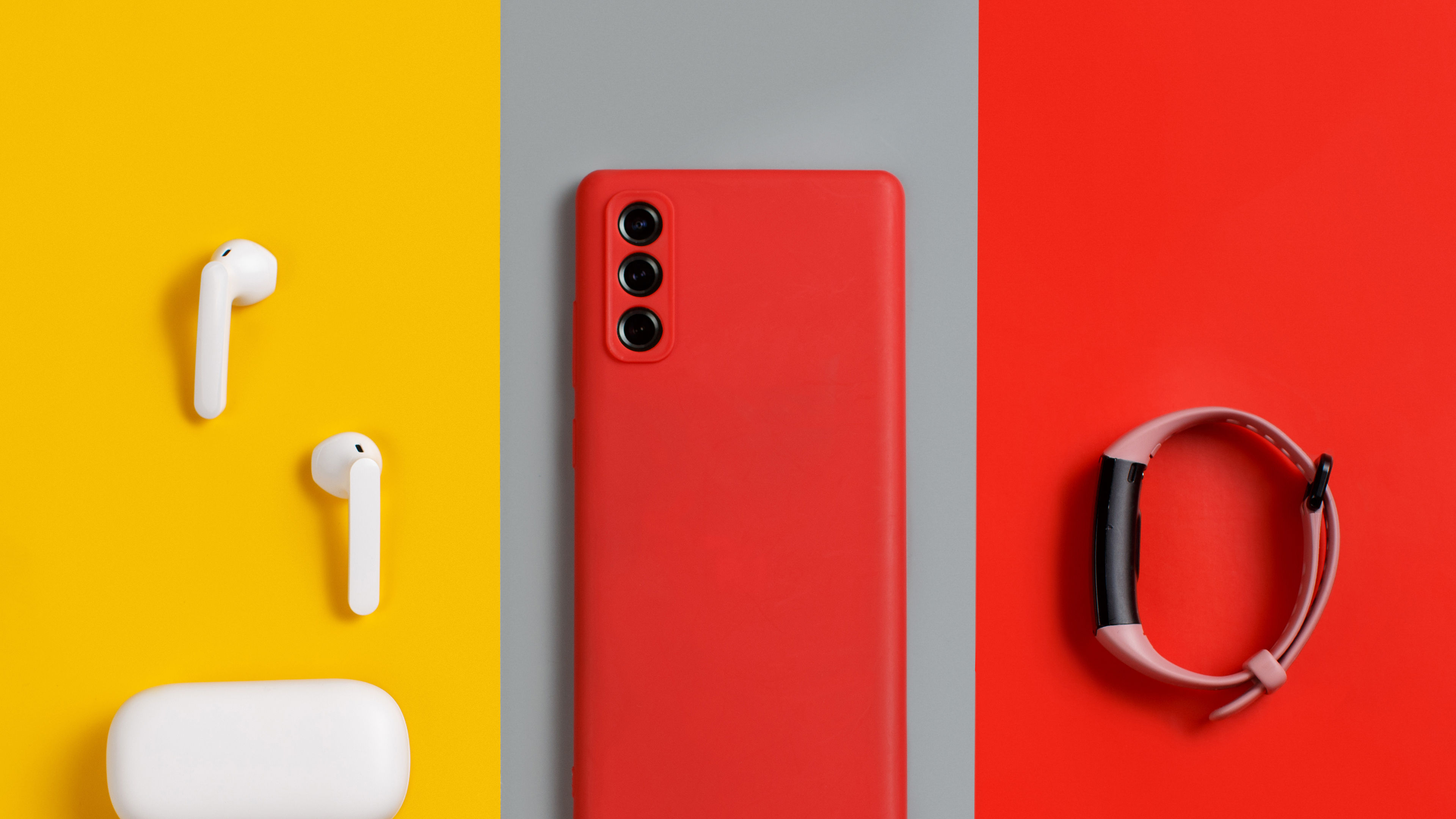 Smartphone, white wireless earphones awith the case and smart watch top view on red, grey and yellow background 