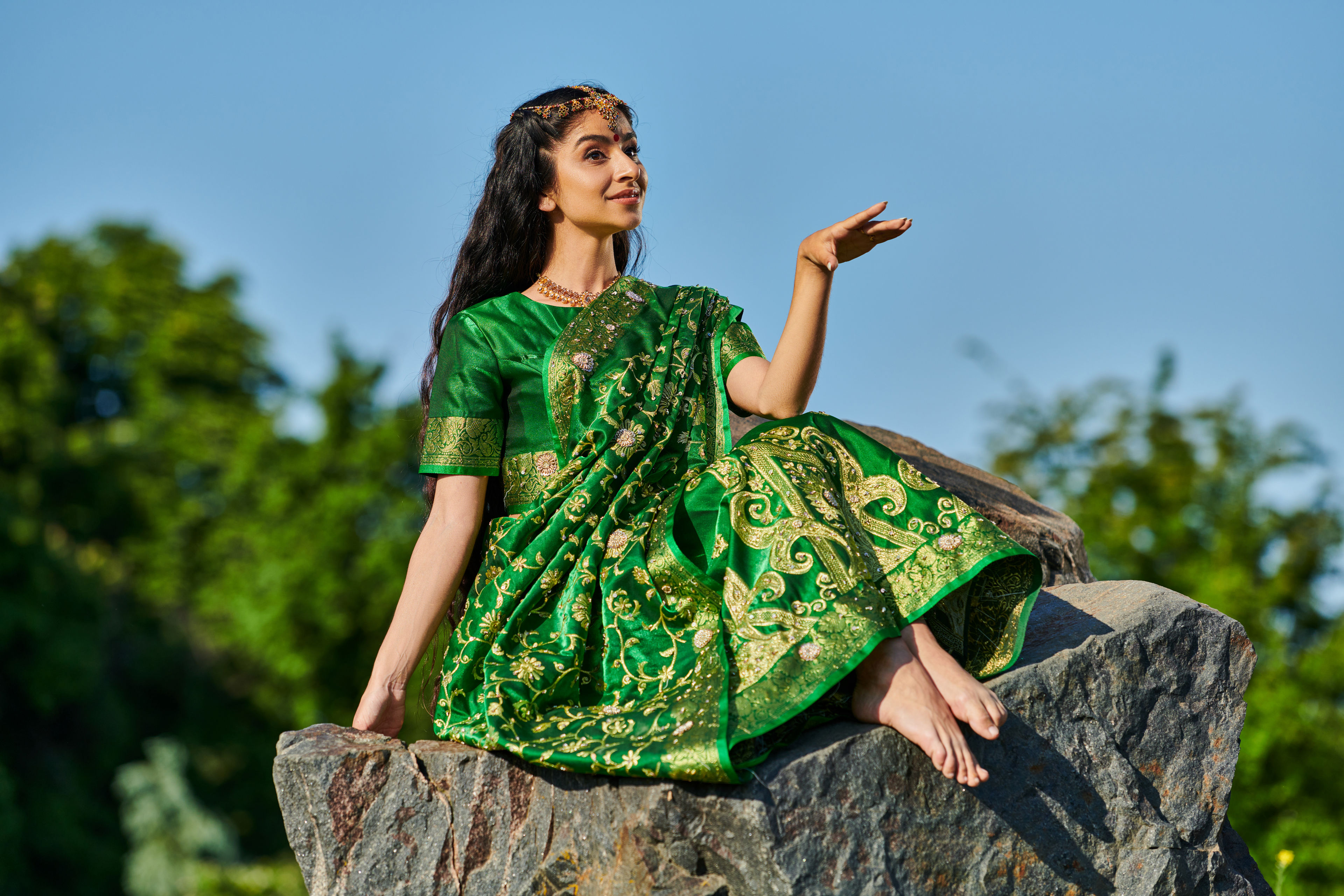 smiling and stylish barefoot indian woman in sari sitting on stone