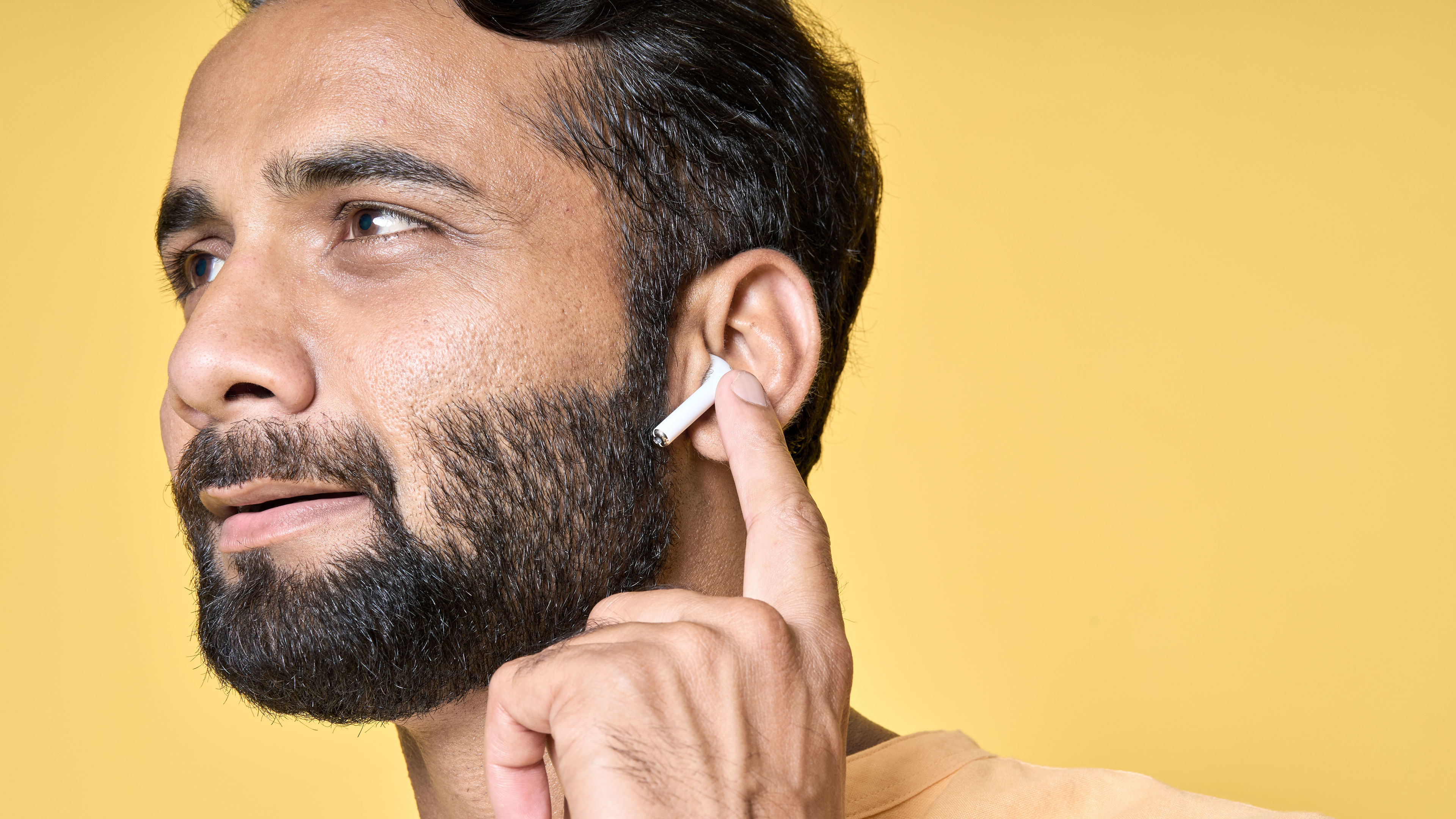 Smiling indian man wearing earbuds listening music or podcast.